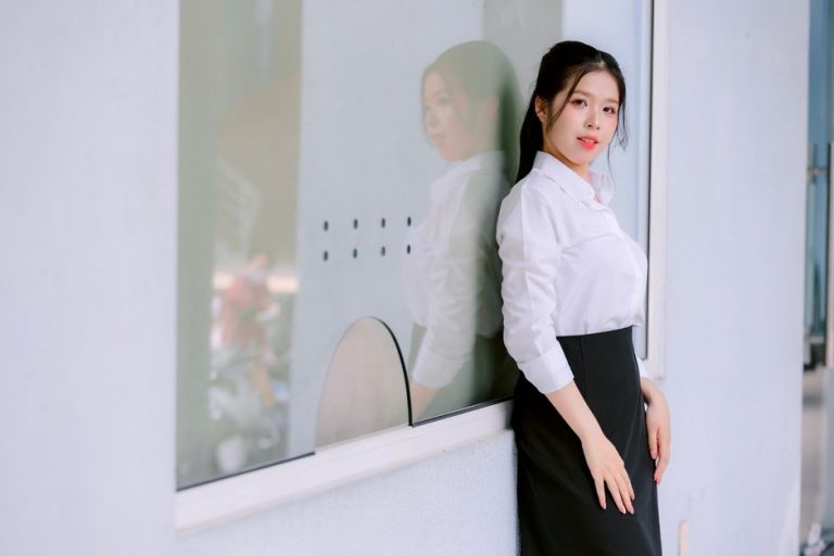 Mujer con camisa blanca y falda midi caminando por la calle en verano con estilo elegante