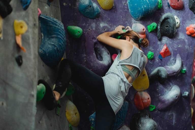 Mujer practicando escalada en rocódromo, ejercicio de fuerza y concentración