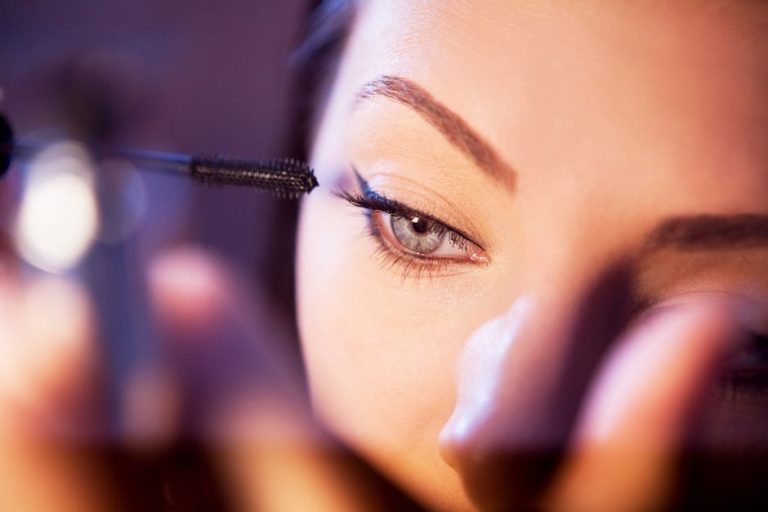 Aplicador de máscara de pestañas marrón con producto cremoso sobre fondo neutro, fotografía de producto de belleza
