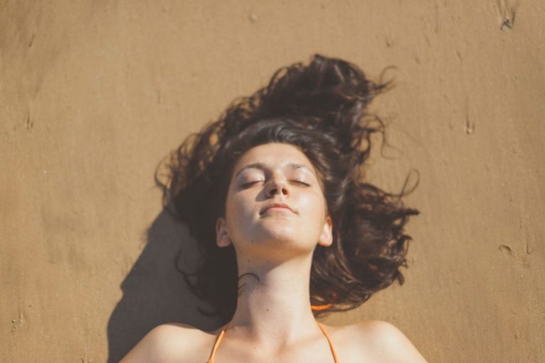 Mujer aclarando el cabello con agua dulce después de un día de playa para prevenir daños