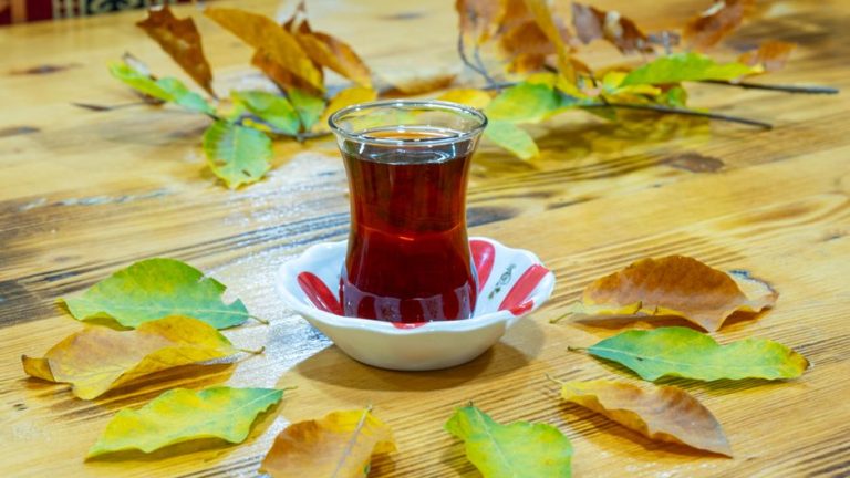 Taza de té verde con hojas sobre mesa de madera, luz natural