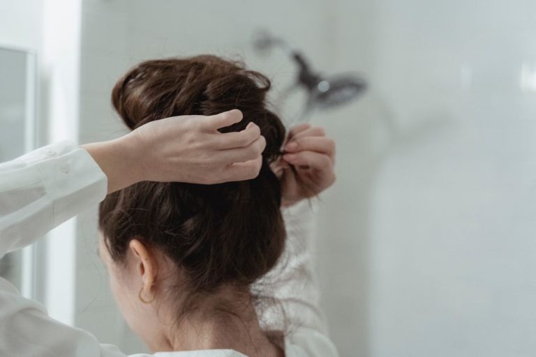 Manos de mujer recogiendo el cabello en un moño pulido, vista desde atrás