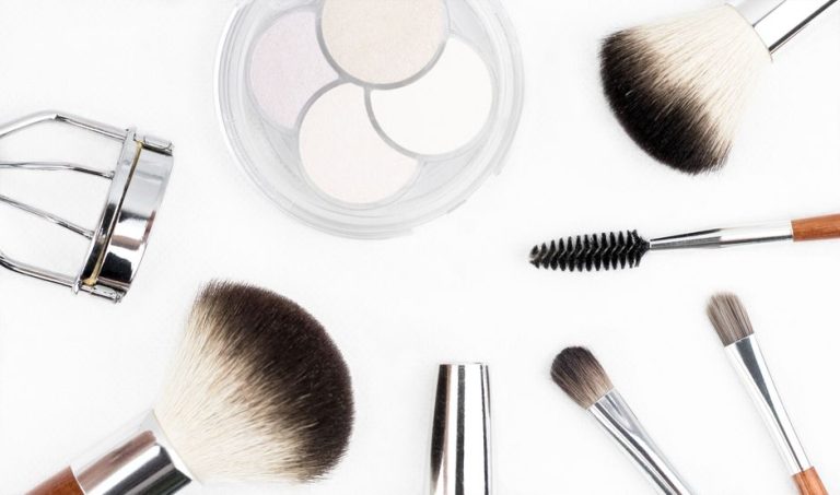 Paleta de sombras de ojos en tonos neutros con brocha sobre mesa de maquillaje