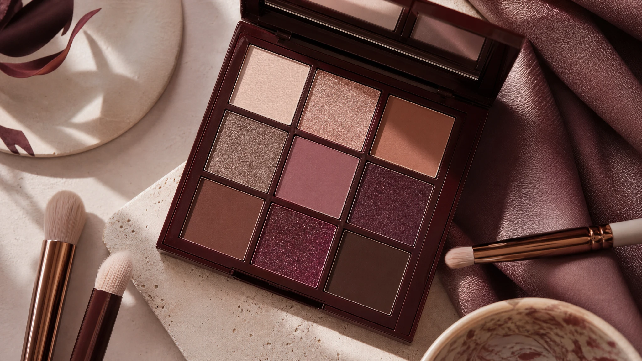 Ilustración editorial de paleta de sombras en tonos neutros y vino con brochas de maquillaje